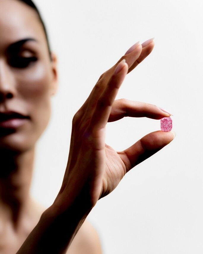 A hand holding a small pink faceted gemstone.